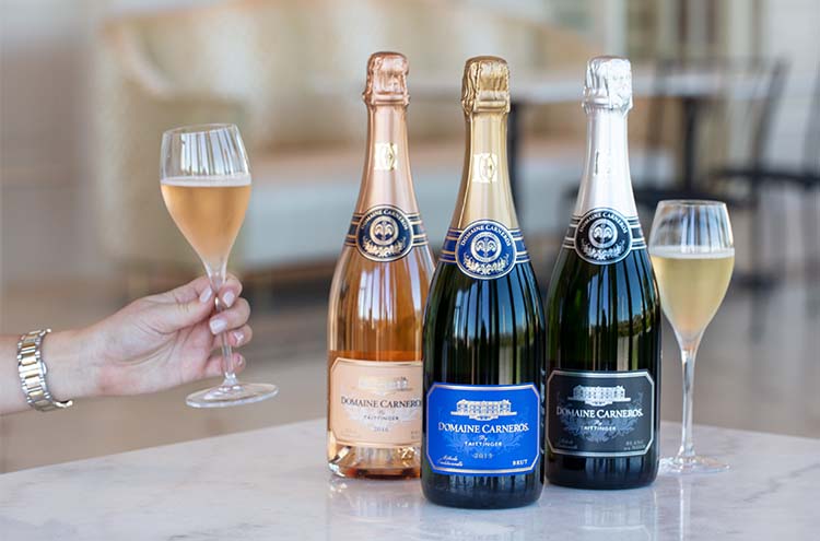 Trio of sparkling wine on marble tabletop and person holding a glass of sparkling wine