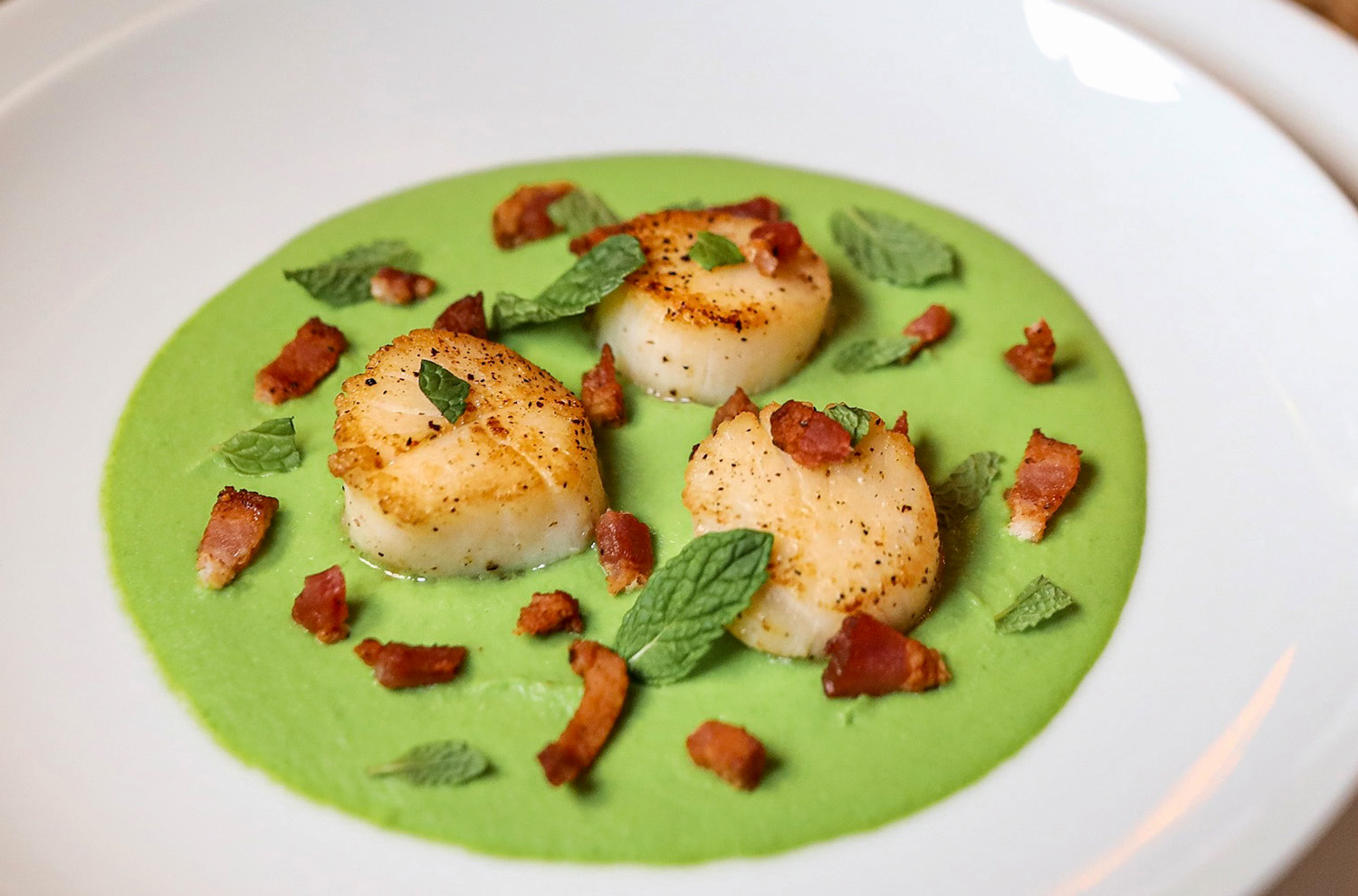 Scallops, Bacon, Mint, Peas on a plated dish.