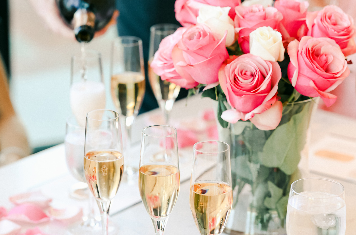 bouquet of pink roses with three sparkling rose flutes being poured