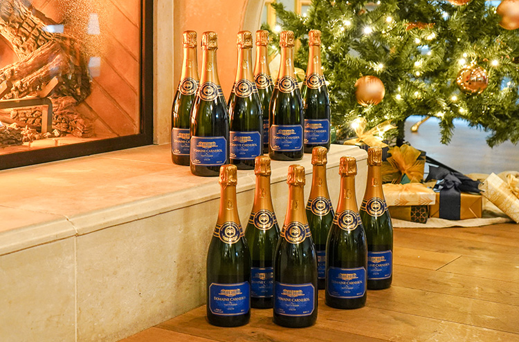 12 bottles of Estate Brut on fireplace in front of Christmas Tree