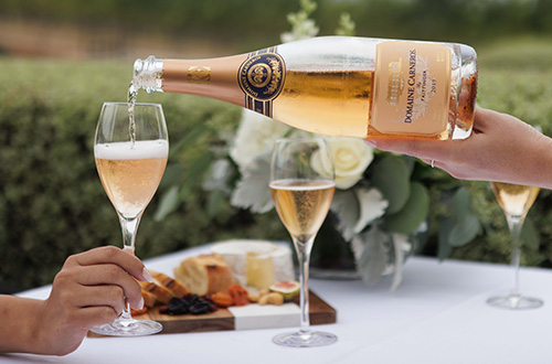 Pouring of sparkling rose into a glass with spring background