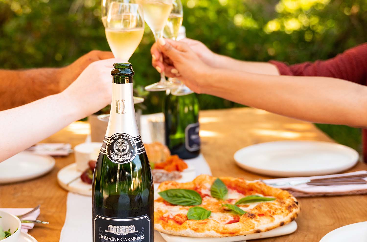 Outdoor table with pizzas and toasting flutes with bottle of sparkling wine